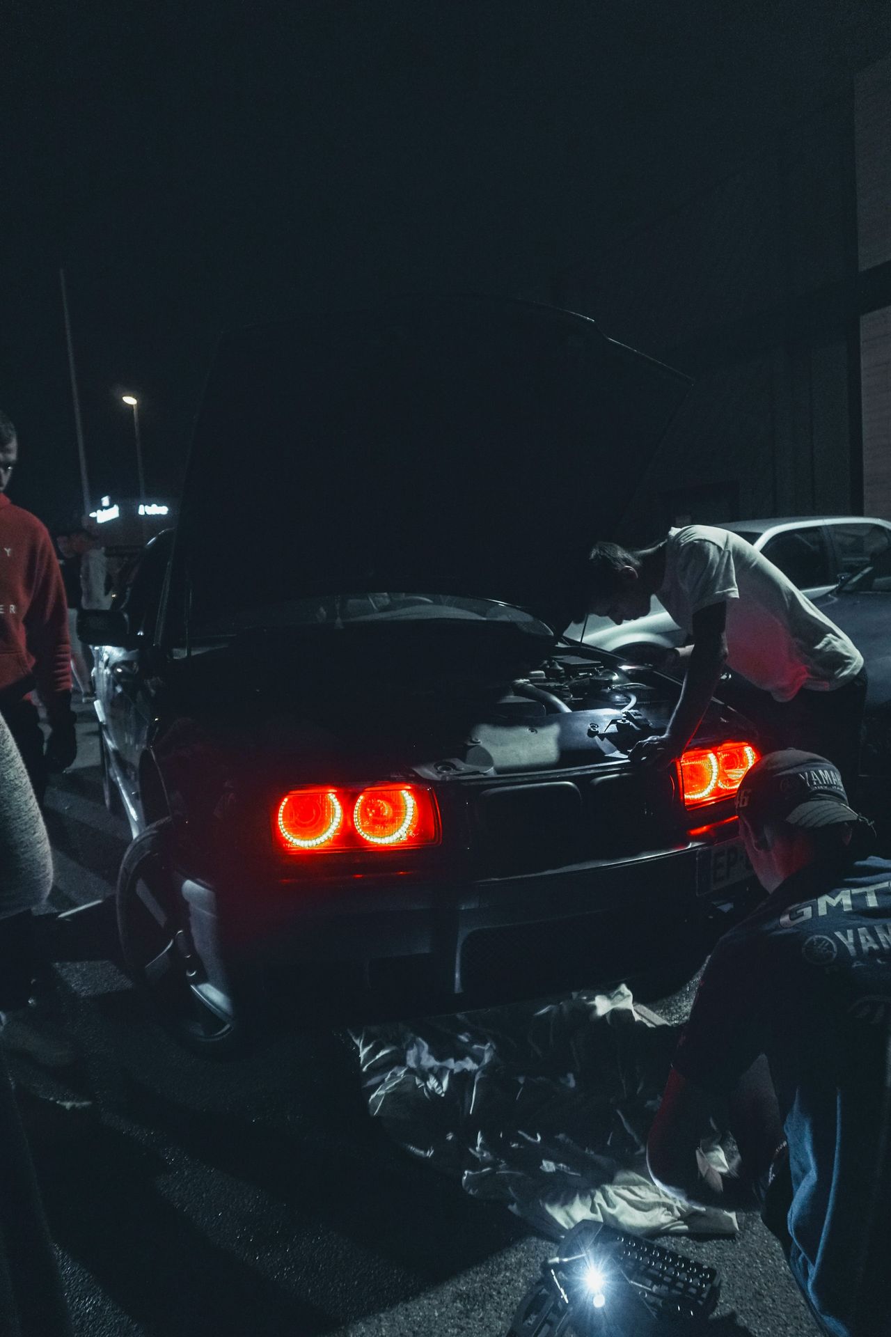 man in red jacket standing beside black car